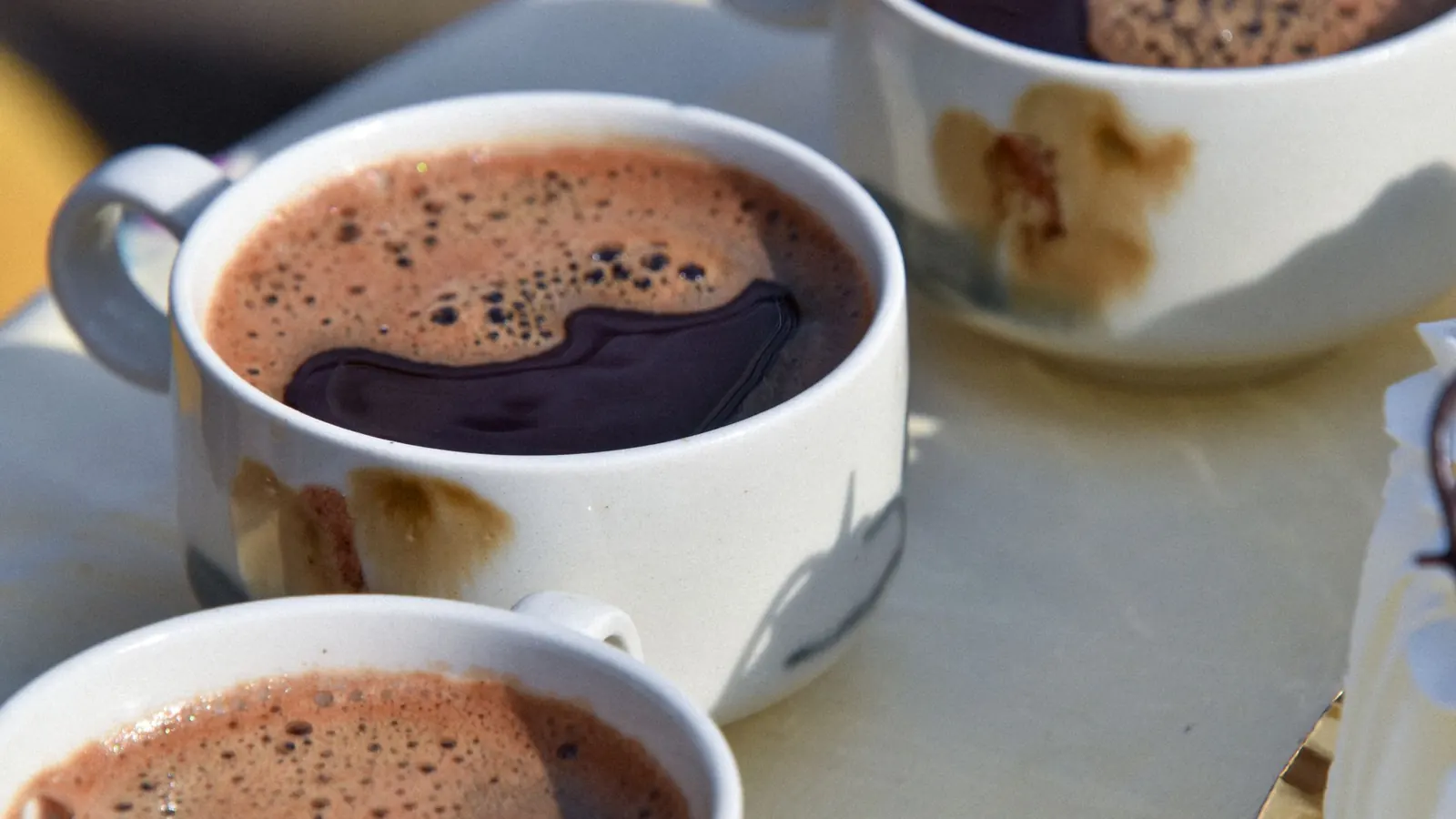Three white cups of frothy hot cocoa on a sunlit table