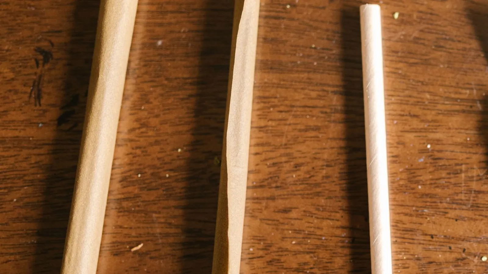 Two pre-shaped paper cones and a thin rolled paper lying side by side on a wooden table